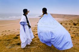 Image du Maroc Professionnelle de  Deux marocains du sud traditionnellement vêtu regardent l'horizon sur les hauteurs de la plage Chbika au environ de Tan Tan durant le grand Moussem. Chaque année la majorité des tribus et des grandes familles nomades du désert se retrouvent sur un site désertique pour célébrer ce grand Moussem où  danse, chants, course de chameaux et fantasia font partie des festivités. , Samedi 18 septembre 2004, ((Photo / Abdeljalil Bounhar) 